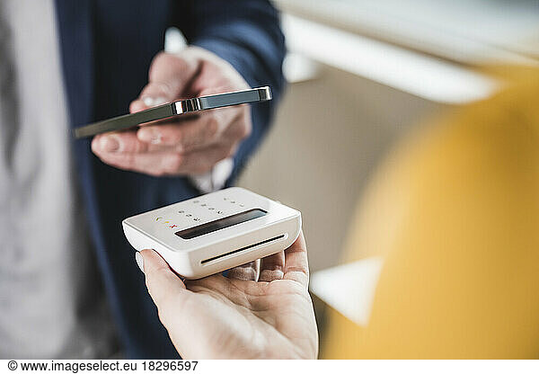Hand of businessman paying with smart phone on card reader machine