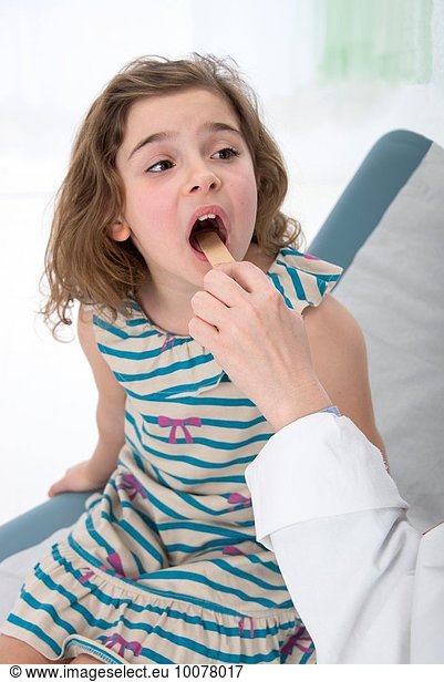Hand of doctor pediatrician examining mouth and throat of little girl with a spatula