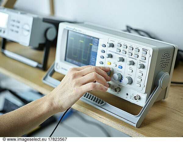 Hand of engineer adjusting oscilloscope in electronic laboratory