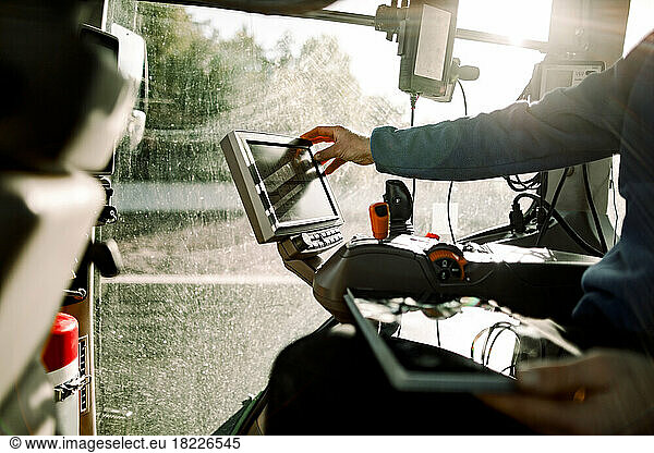 Hand of farmer operating computer sitting in tractor on sunny day