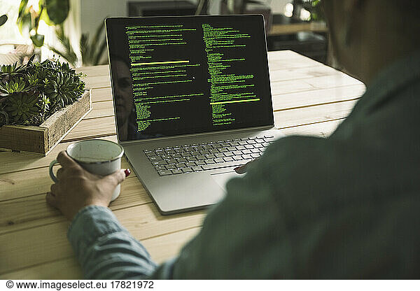 Hand of freelance computer programmer holding coffee cup at table working in home office