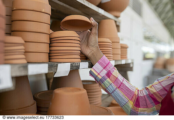 Hand of gardener stacking clay saucers on shelf in warehouse
