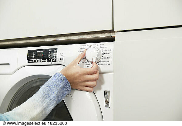 Hand of girl adjusting knob on washing machine at home