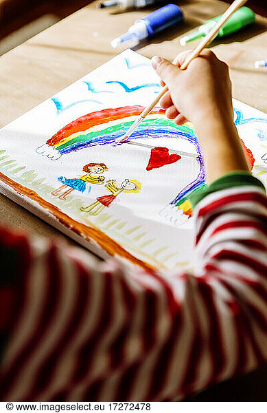 Hand of girl painting rainbow over table at home