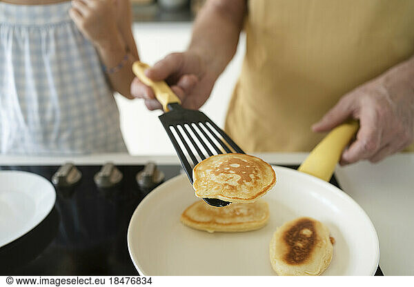 Hand of grandfather flipping pancake using spatula in kitchen at home