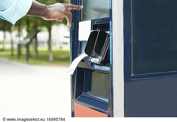 Hand of male commuter using ticket machine on sunny day
