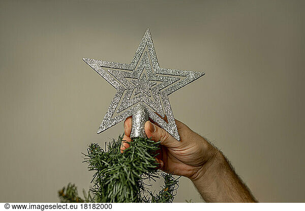 Hand of man decorating Christmas tree with silver star