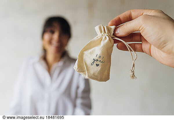 Hand of man giving small gift to woman standing in background