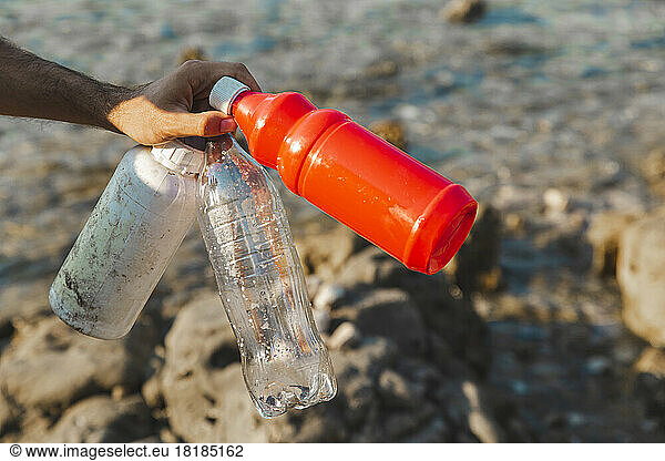 Hand of man holding empty plastic bottles at beach