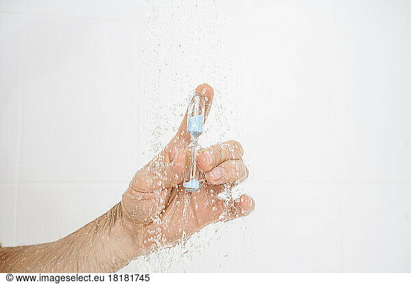 Hand of man holding hourglass in water under shower