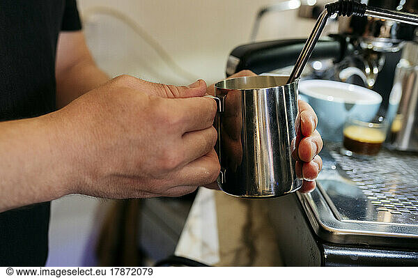 Hand of man holding mug making coffee in cafe