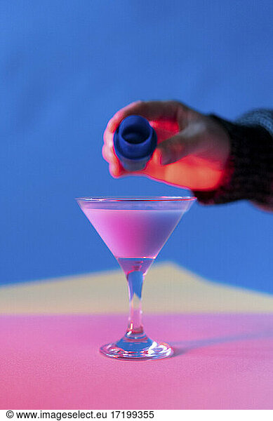 Hand of man pouring blue liquid into martini glass with pink liquid