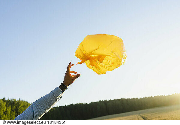 Hand of man reaching towards garbage bag balloon at field