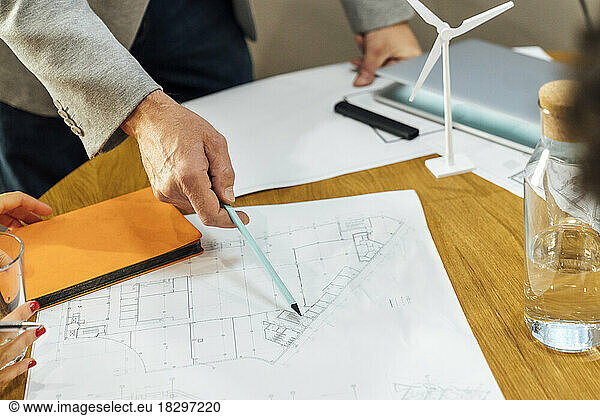 Hand of mature businessman pointing with pen on blueprint at office