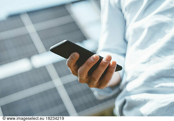 Hand of mature man using smart phone by solar panels