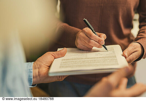 Hand of mature woman filling form with pen