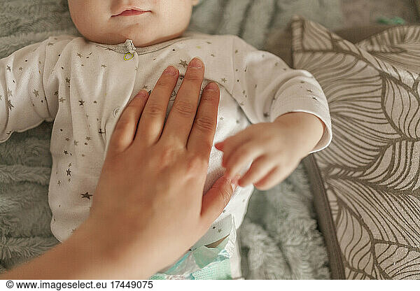 Hand of mother on chest of small baby infant who is lying on bed