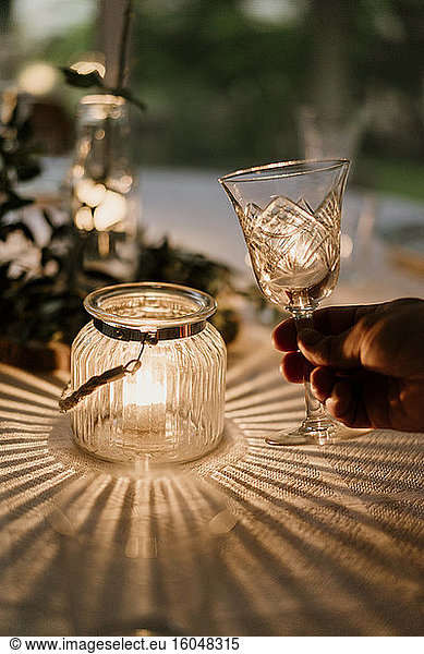 Hand of person holding wineglass in front of burning candle covered with glass bowl