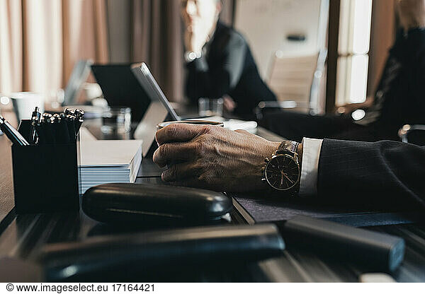 Hand of senior businessman holding coffee cup at conference table in board room during meeting