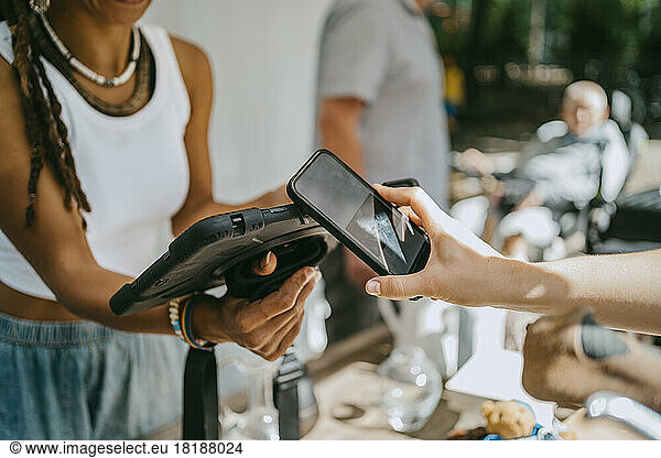 Hand of woman doing contactless payment while shopping at flea market
