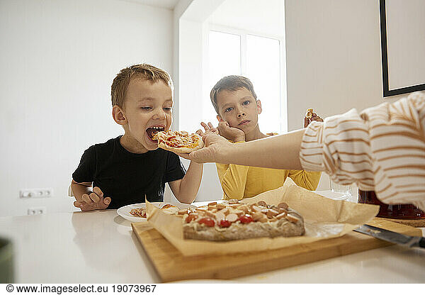 Hand of woman feeding pizza to son at home