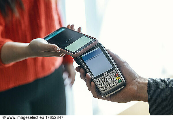 Hand of woman making contactless payment through mobile phone