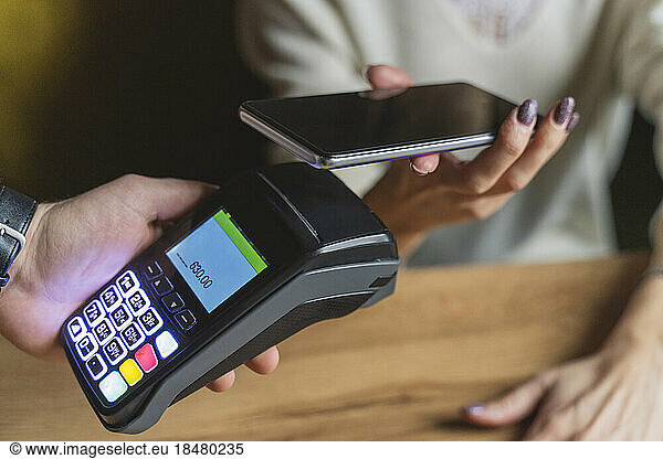 Hand of woman making payment through smart phone at cafe