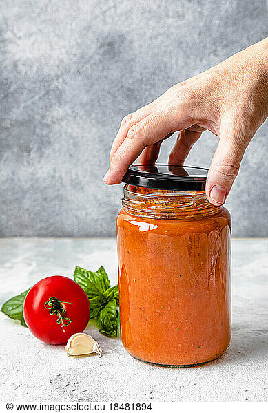 Hand of woman opening tomato sauce jar's lid
