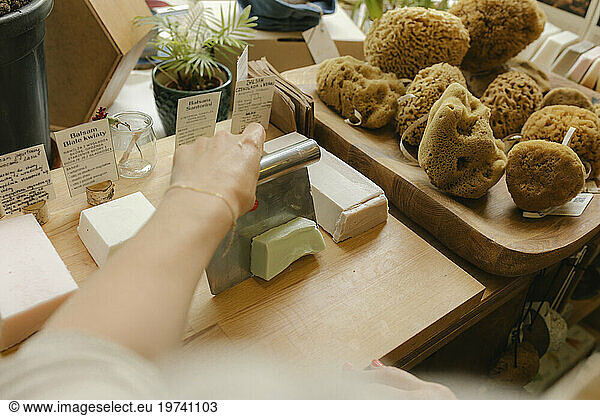 Hand of woman owner cutting bar of soap on table in store