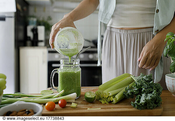 Hand of woman pouring smoothie in mason jar from juicer at home