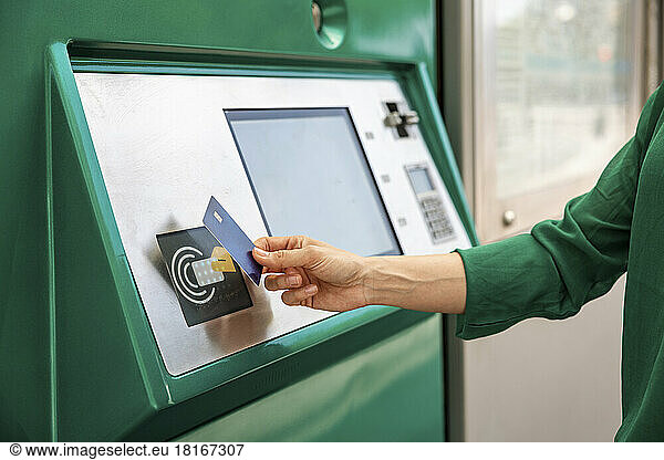 Hand of woman tapping credit card on ticket machine at tram stop