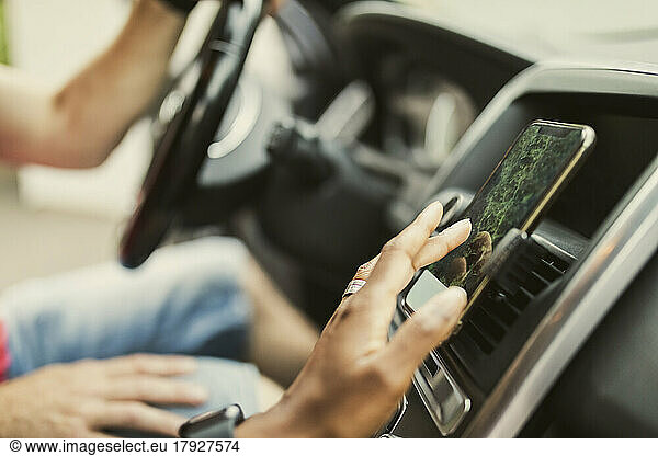 Hand of woman using GPS through smart phone attached on dashboard in car