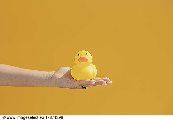 Hand of woman with rubber duck in front of yellow wall