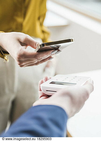 Hand of young businesswoman paying through smart phone on credit card reader