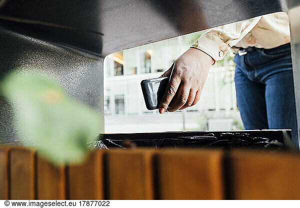 Hand of young businesswoman throwing smart phone into garbage bin