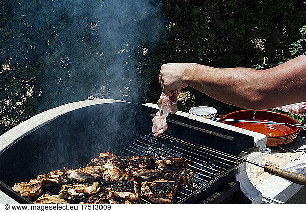 Hand of young man placing meat on barbecue grill in yard