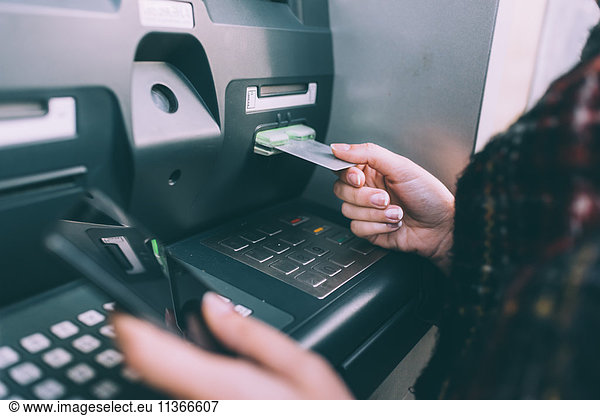 Hand of young woman inserting credit card into cash machine