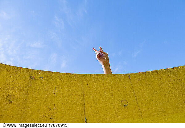 Hand of young woman showing peace gesture in front of blue sky