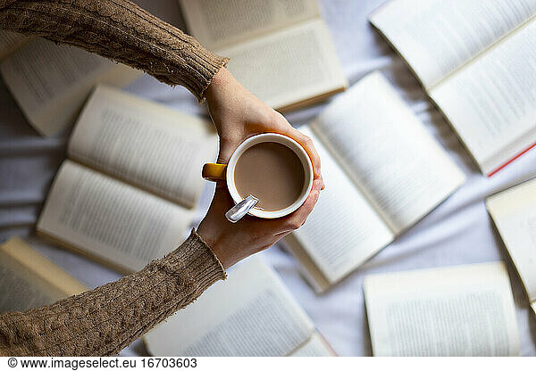 Hand picking up a cup of warm coffee with books.