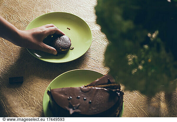 Hand picks up small round chocolate cake on plate