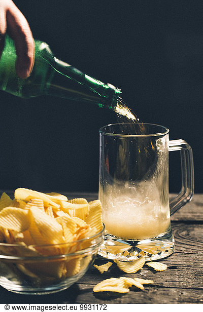 Hand pouring glass of beer near potato chips