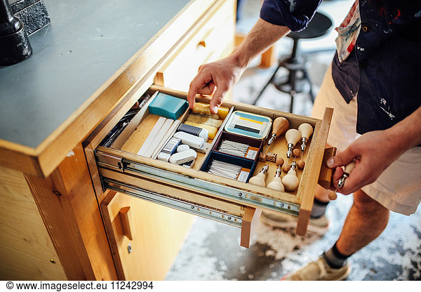 Hand reaching into open drawer containing equipment and materials in book arts workshop