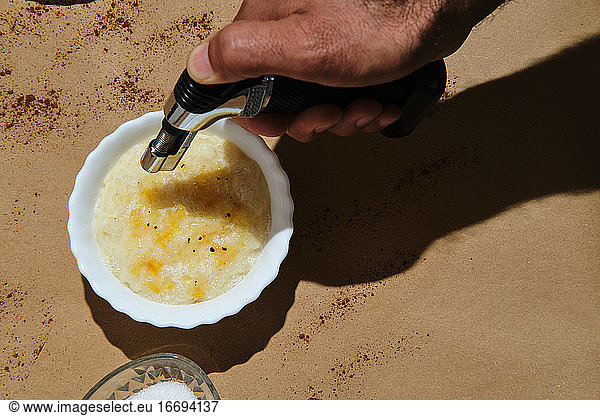 hand with burner to burn the sugar on the rice pudding on a brown back