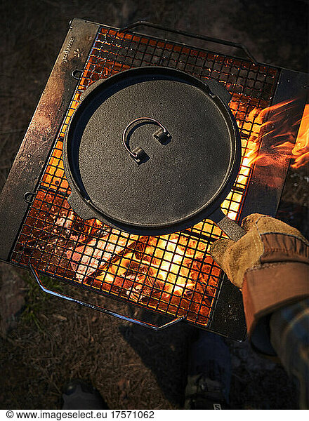 Hands adjusting a cast iron pan over an open fire.