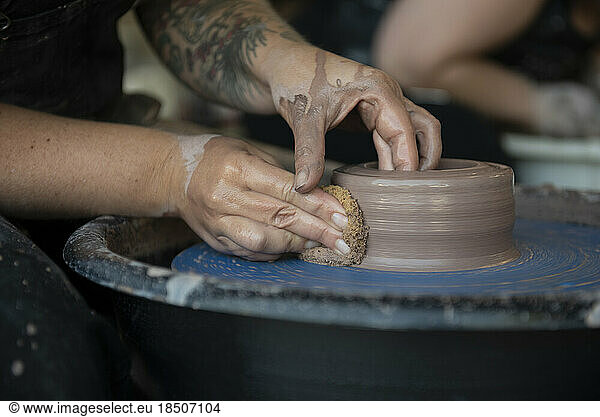 Hands crafting a pot on pottery wheel