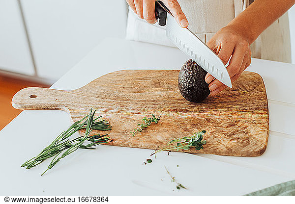 Hands cutting hass avocado on cutting board with rosemary and thyme