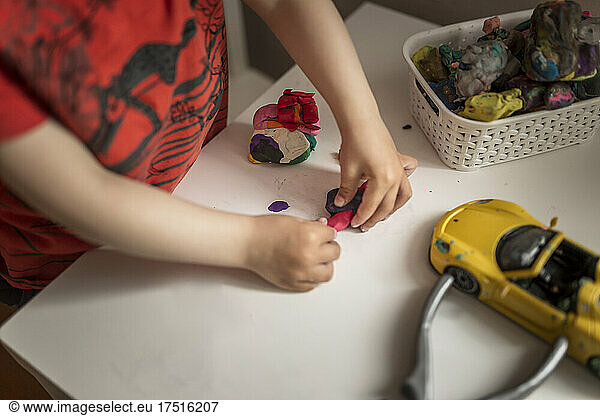 Hands of a child playing with play doh on white table