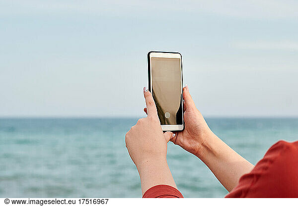 Hands of a person holding a mobile with the sea in the background