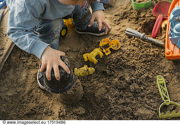 Hands of boy playing in sandpit and making mud pie