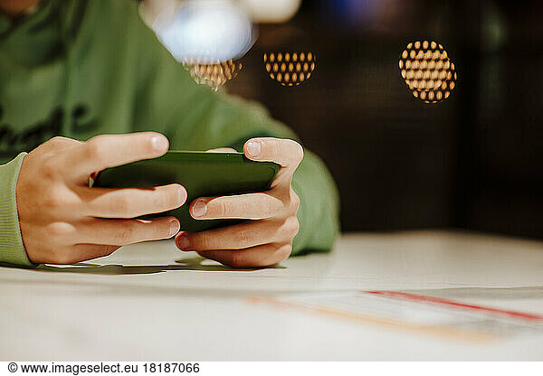 Hands of boy using smart phone at table in food court
